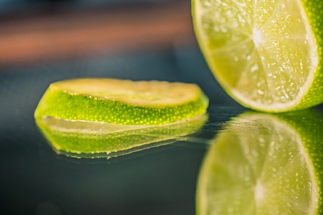 Close-up of a sliced lime on a reflective surface, with one slice in focus and part of the remaining lime visible in the background.