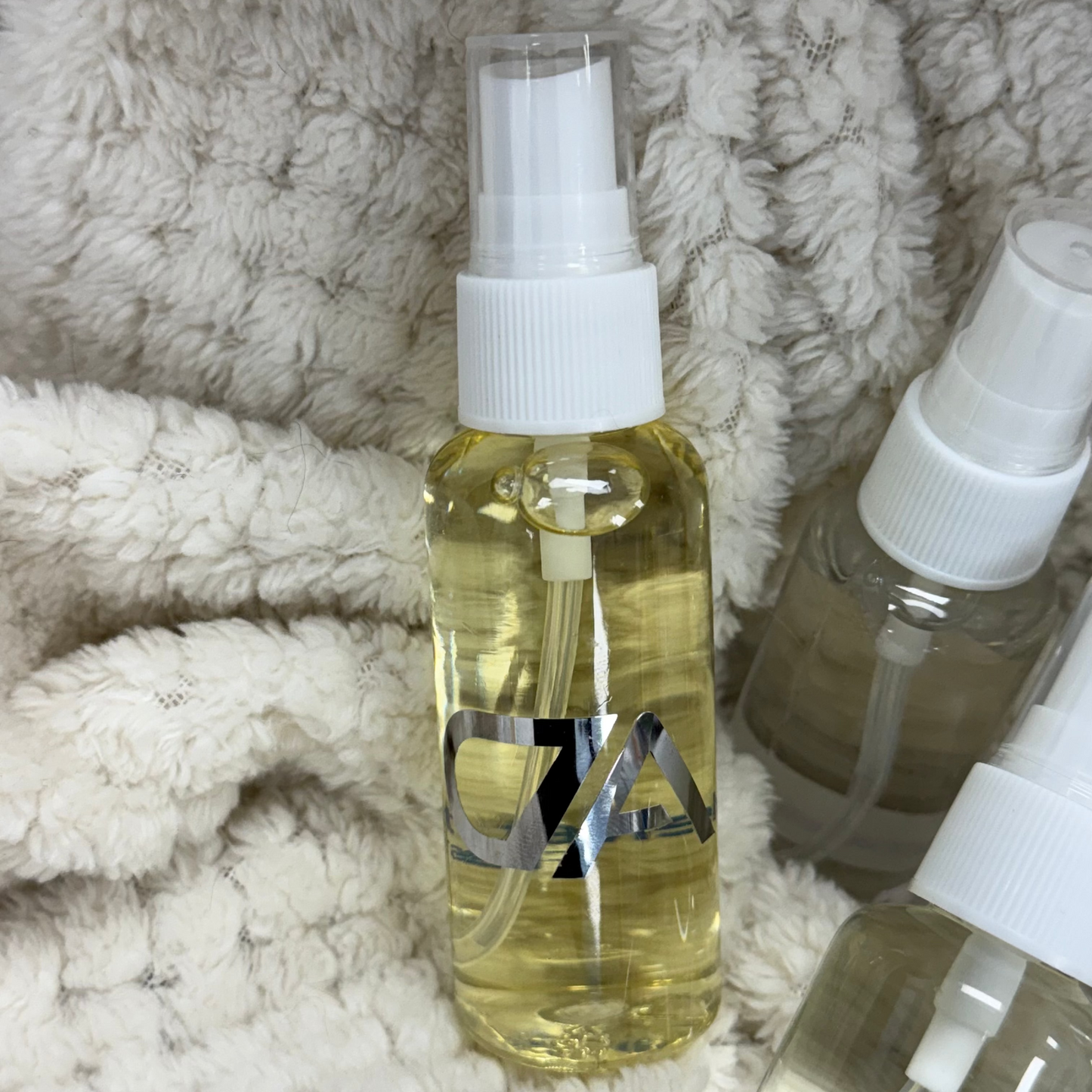 The Mini Room Spray, featuring a clear plastic bottle with a white pump and light yellow liquid, rests on textured off-white fabric—ideal for travel-friendly freshness anywhere.
