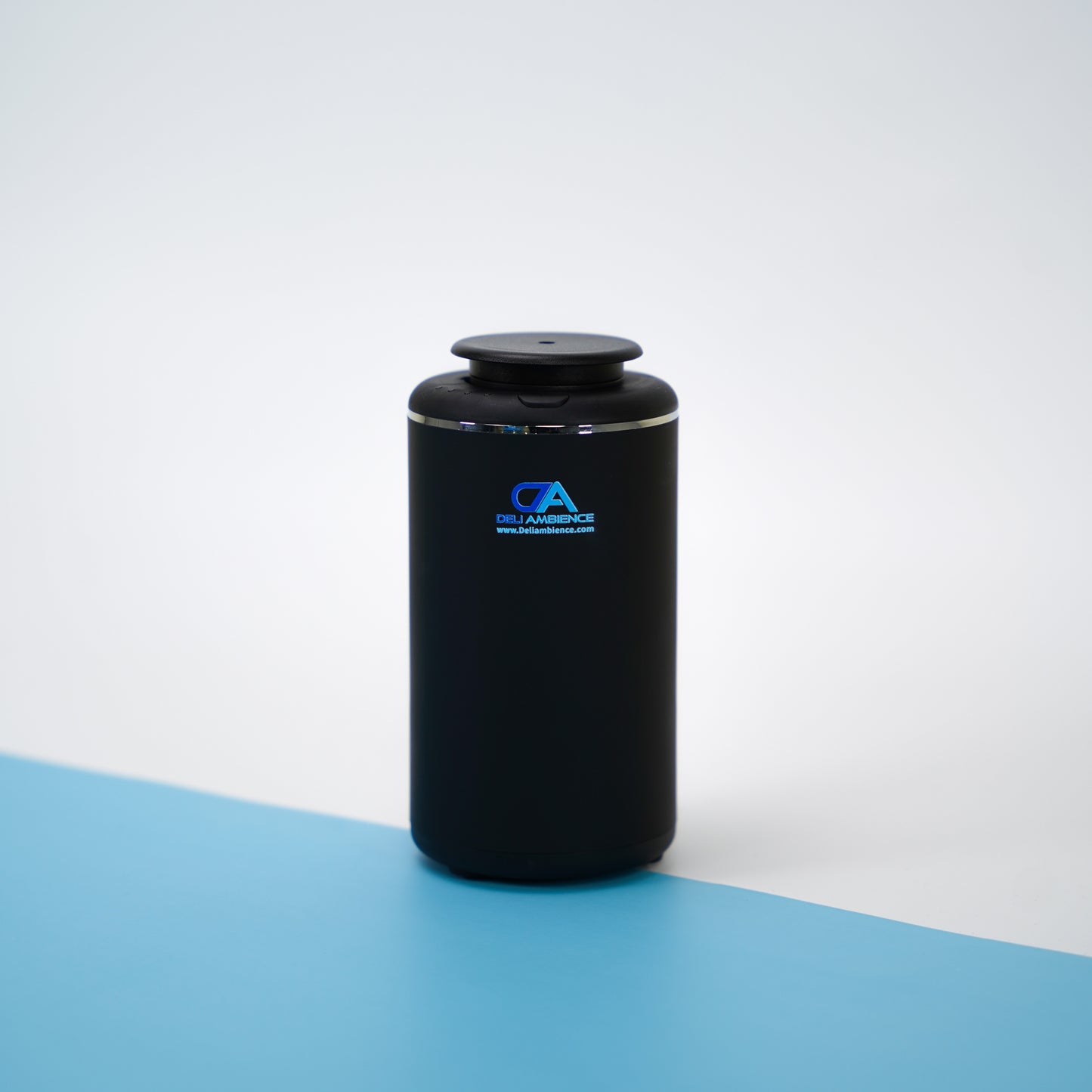 The Venus Compact Oil Diffuser USB-C Power, designed in a sleek black finish with a logo, sits elegantly on a blue and white surface, making it ideal for small spaces or on-the-go use.