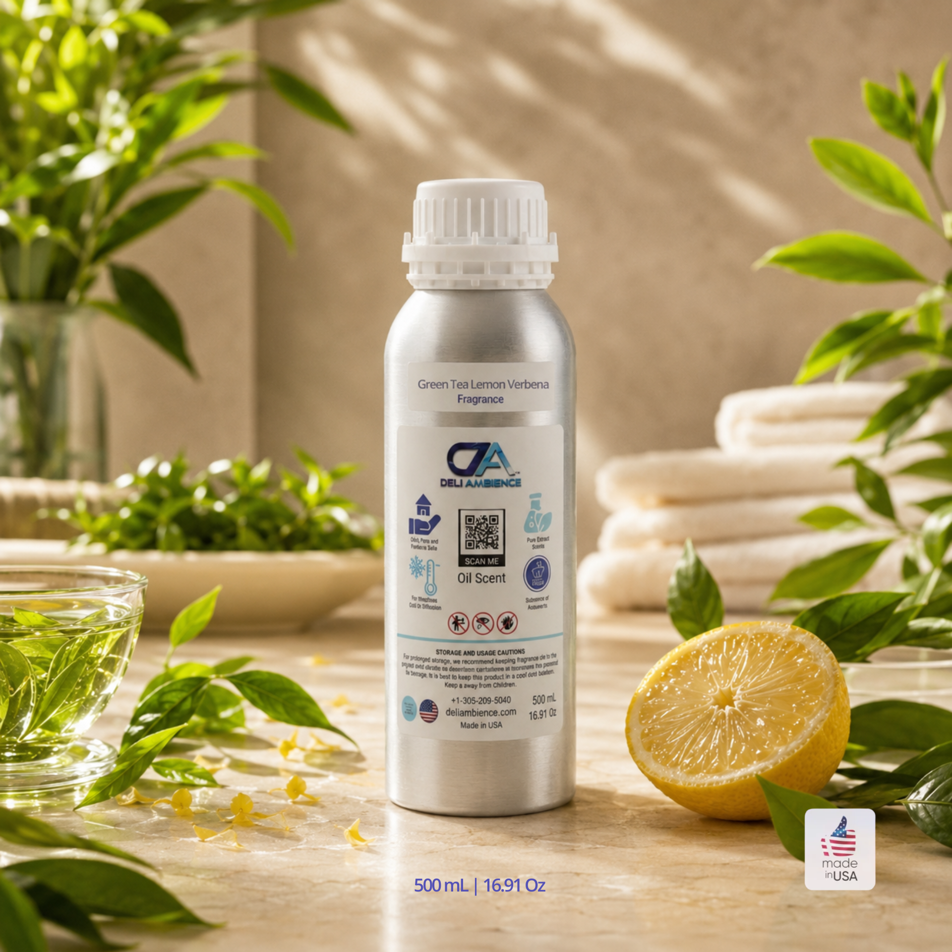 A 500 mL silver bottle of Green Tea Lemon Verbena Oil Scent is displayed with green tea leaves, citrus peel, lemon half, a glass bowl, and rolled white towels on a wooden surface.