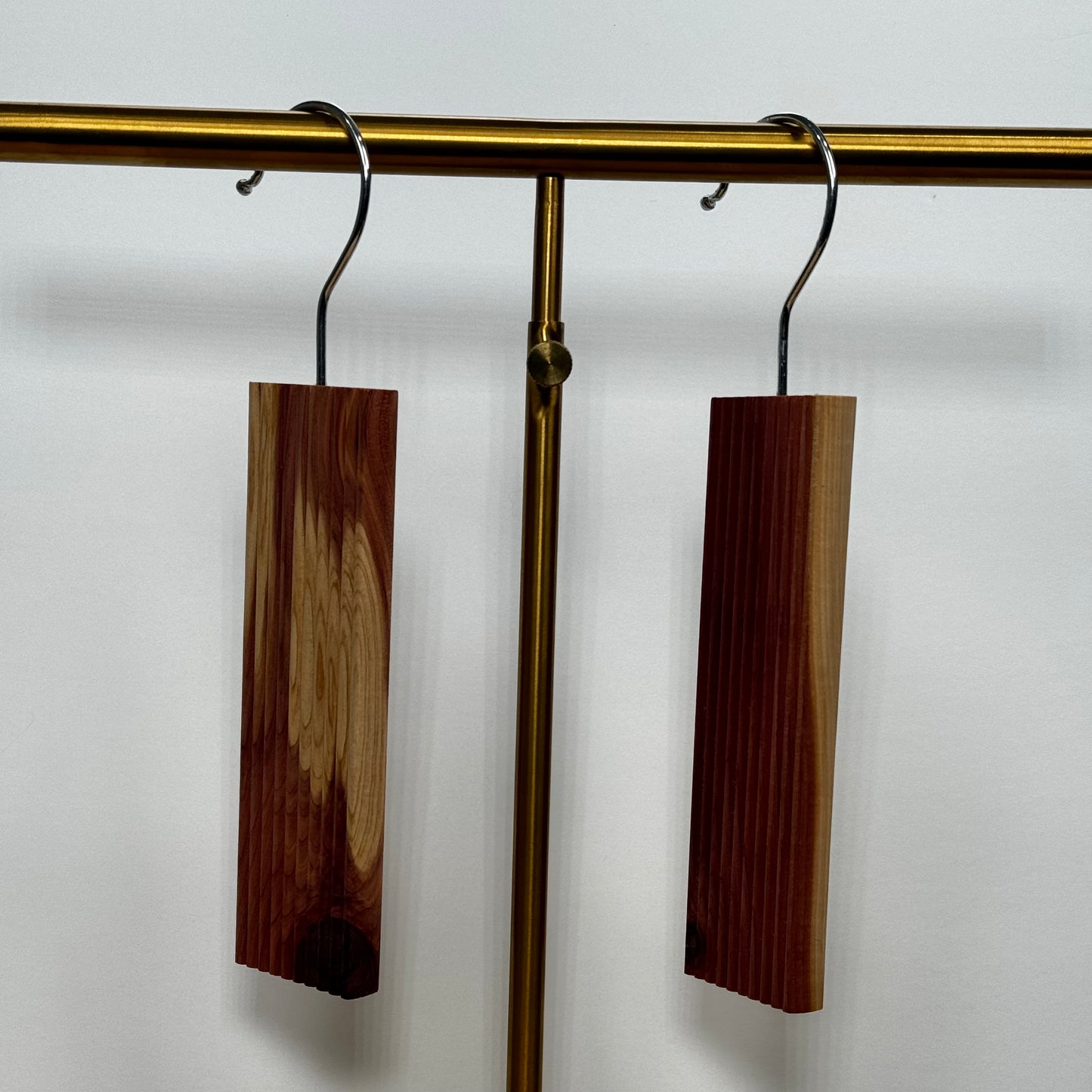 Two Scented Cedar Wood Hangups with Hook for Closets on a gold rack against a white wall.