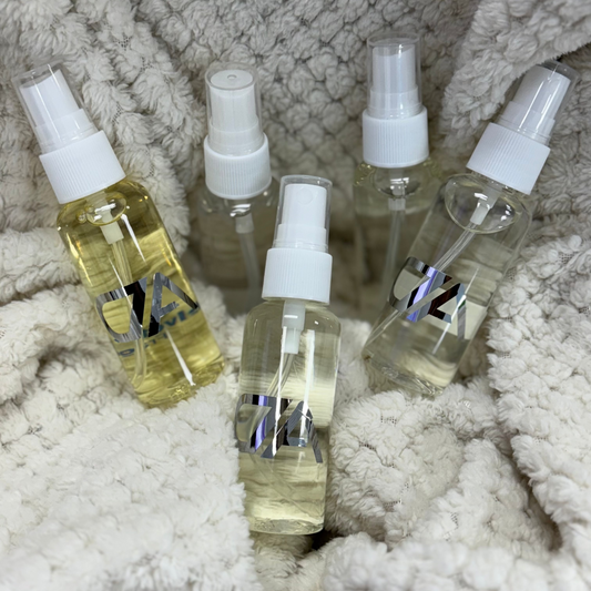 Five Mini Room Spray bottles—three with clear liquid, two with yellow—are arranged on a textured off-white blanket. Each portable spray features a silver and black logo, making them perfect for travel and everyday use.