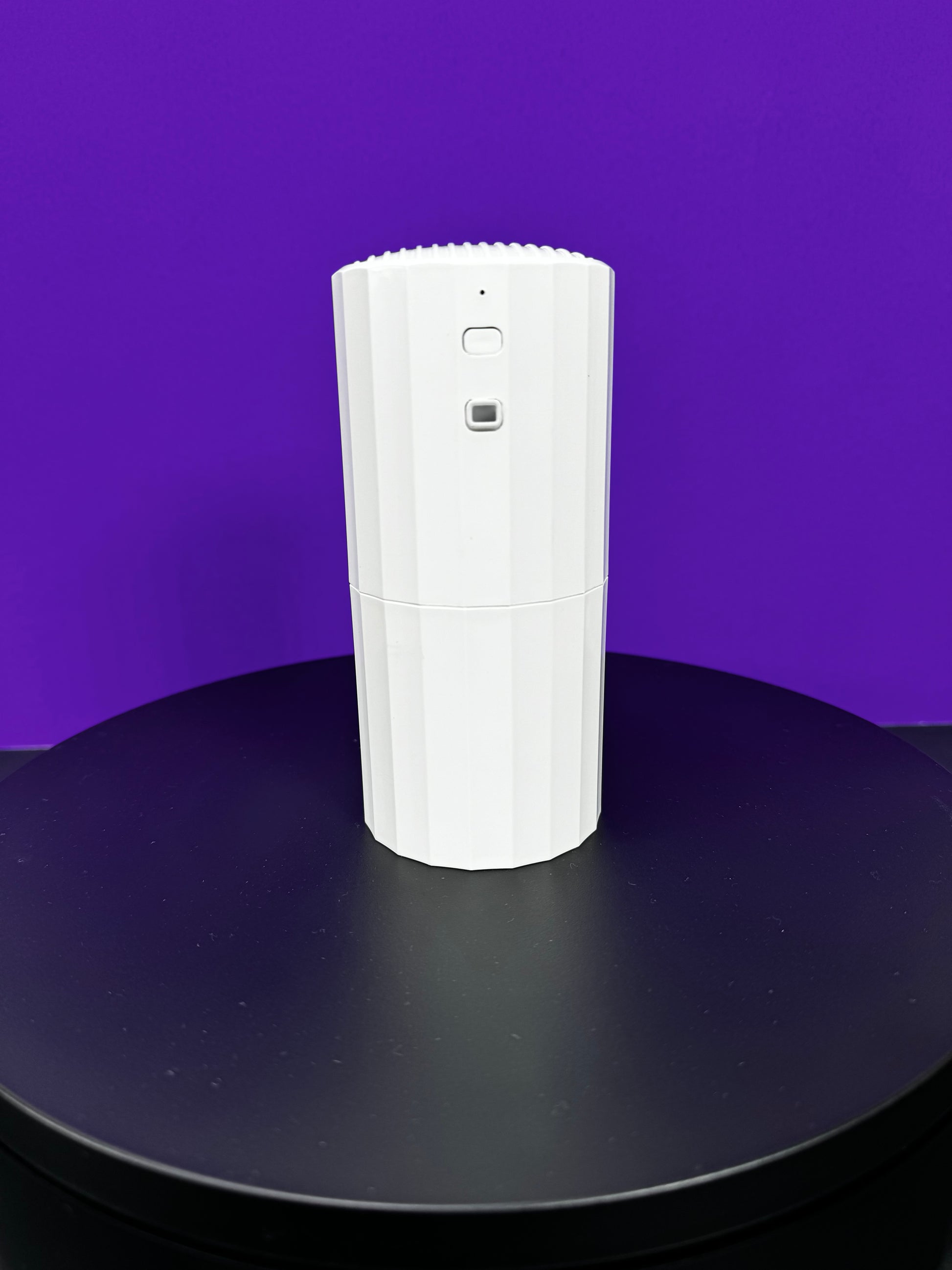 DA Plug In Scent Diffuser sitting on a table in front of a purple wall.