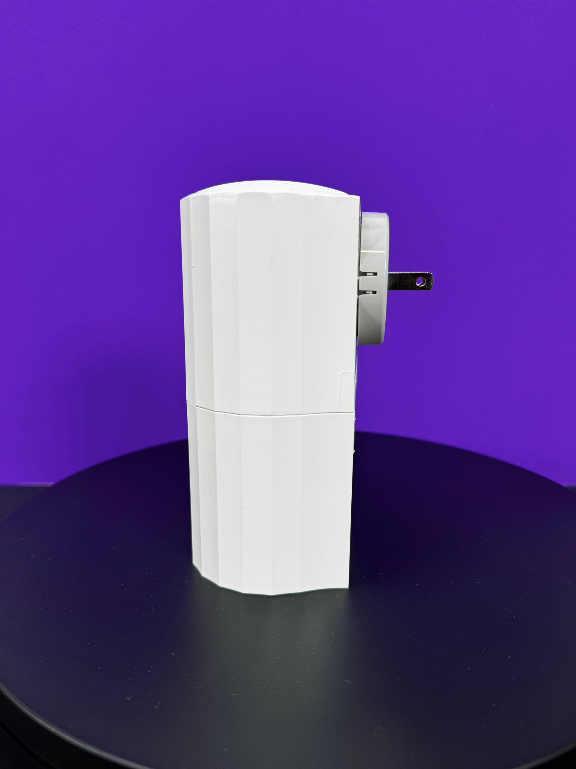 A white box sitting on a table against a purple background; it is a DA Plug In Scent Diffuser for a waterless solution.
