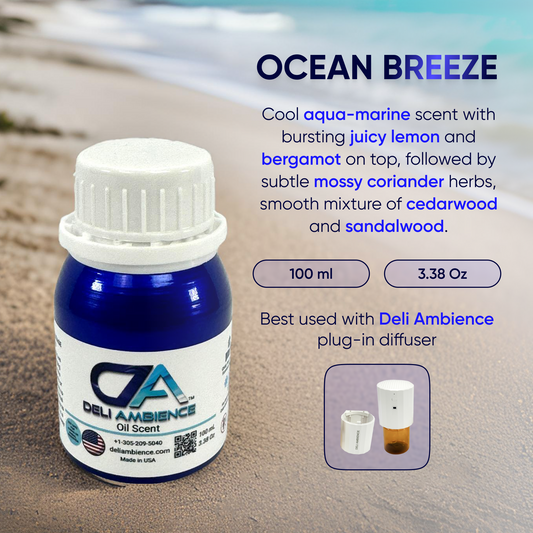 A bottle of Deli Ambience "DA Ocean Breeze" Oil Scent 100 ML stands on a sandy beach. Text describes its refreshing aroma, size (100 ml/3.38 oz), and suggests use with a Deli Ambience plug-in diffuser, ensuring high-quality ingredients for an authentic coastal experience.