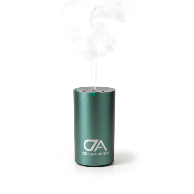 A green cylindrical device labeled "Nefeli Oil Diffuser" emits visible vapor from its top, highlighting a sleek cold-air essential oil diffuser set against a plain white background.