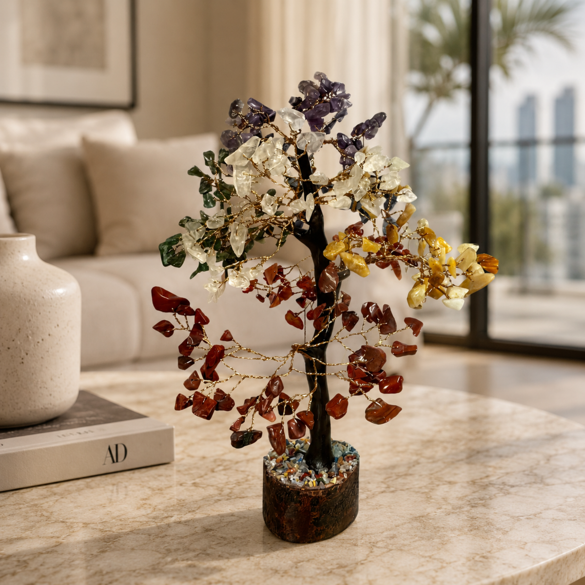 The Chakra Tree, a decorative sculpture with multicolored crystal stone leaves, sits on a marble table in a modern living room, bringing an elegant touch of Feng Shui to the space.