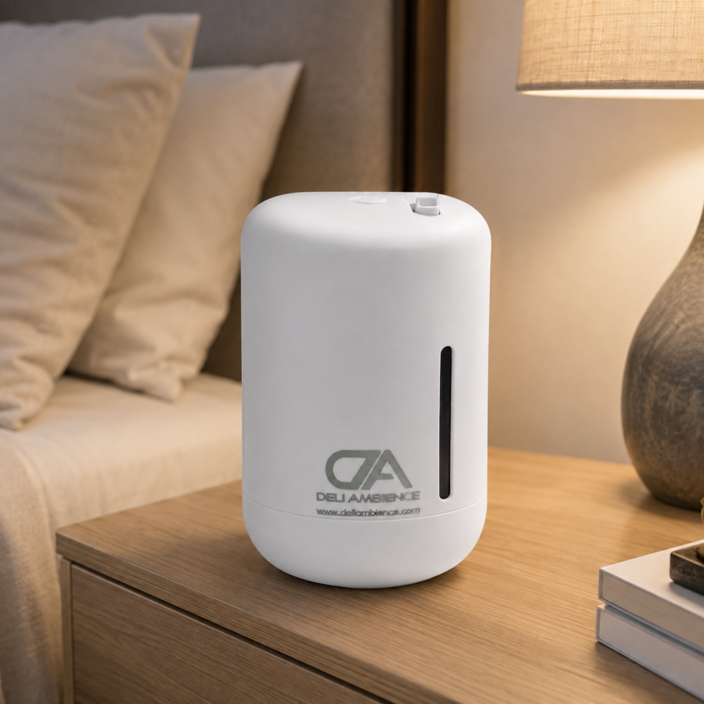 The Afrodita Scent Diffuser sits on a wooden nightstand next to a bed and a table lamp, making it the perfect diffuser for small spaces.