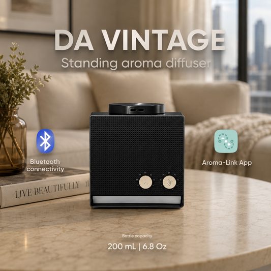 A sleek black DA Vintage Diffuser with Sea Water Oil (100 ml) sits on a table, with on-screen text highlighting Bluetooth connectivity, app control, and its 100 ml capacity. Infusing your space with a calming sea-inspired fragrance, the diffuser is set against a window framing a vibrant cityscape.